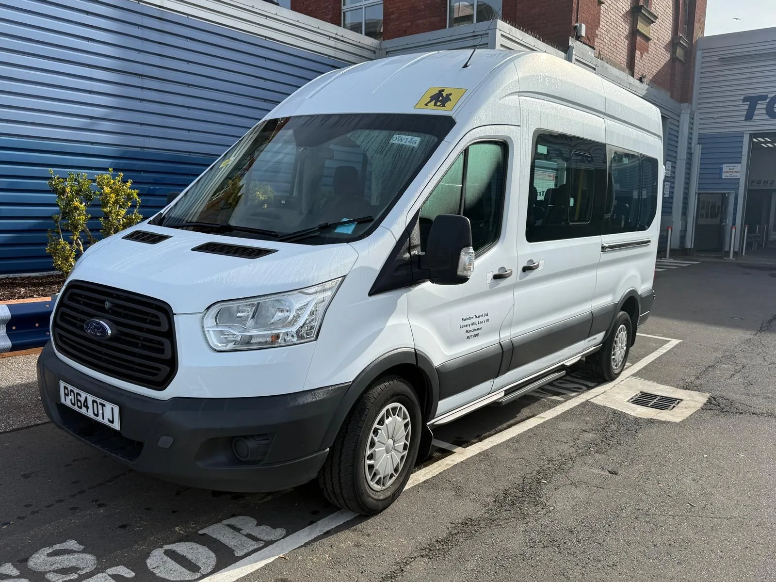 White 14 seater Ford Transit minibus parked in a marked bay, seen from the front three-quarter angle