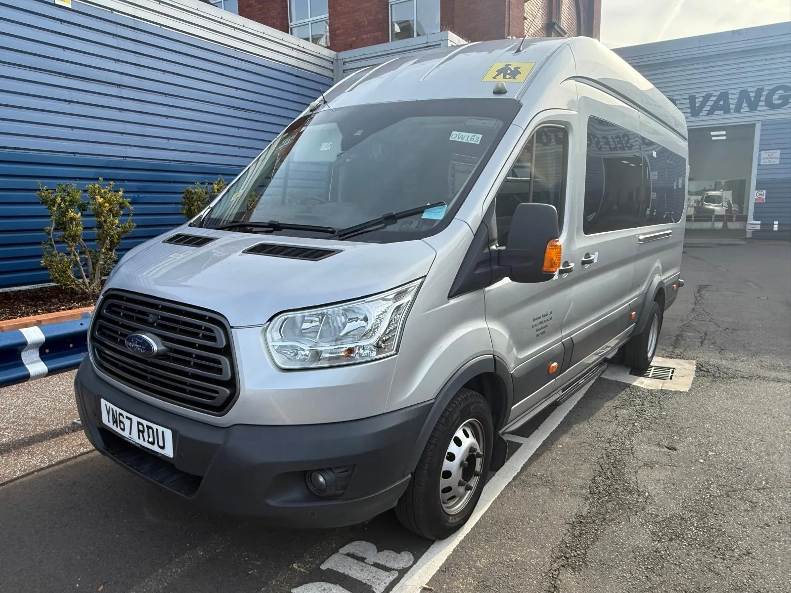 Silver 16 seater Ford Transit minibus with a school bus sign, viewed from the front three-quarter angle