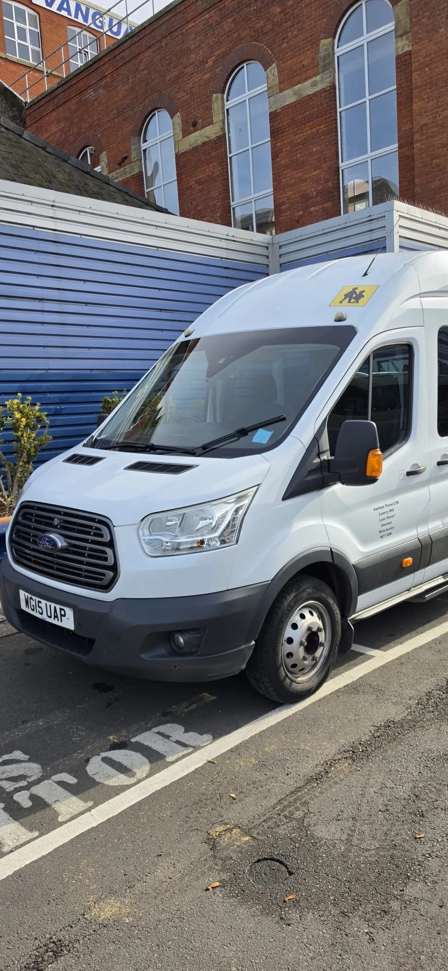 White 17 seater Ford Transit minibus parked by a red brick building, seen from the front three-quarter
