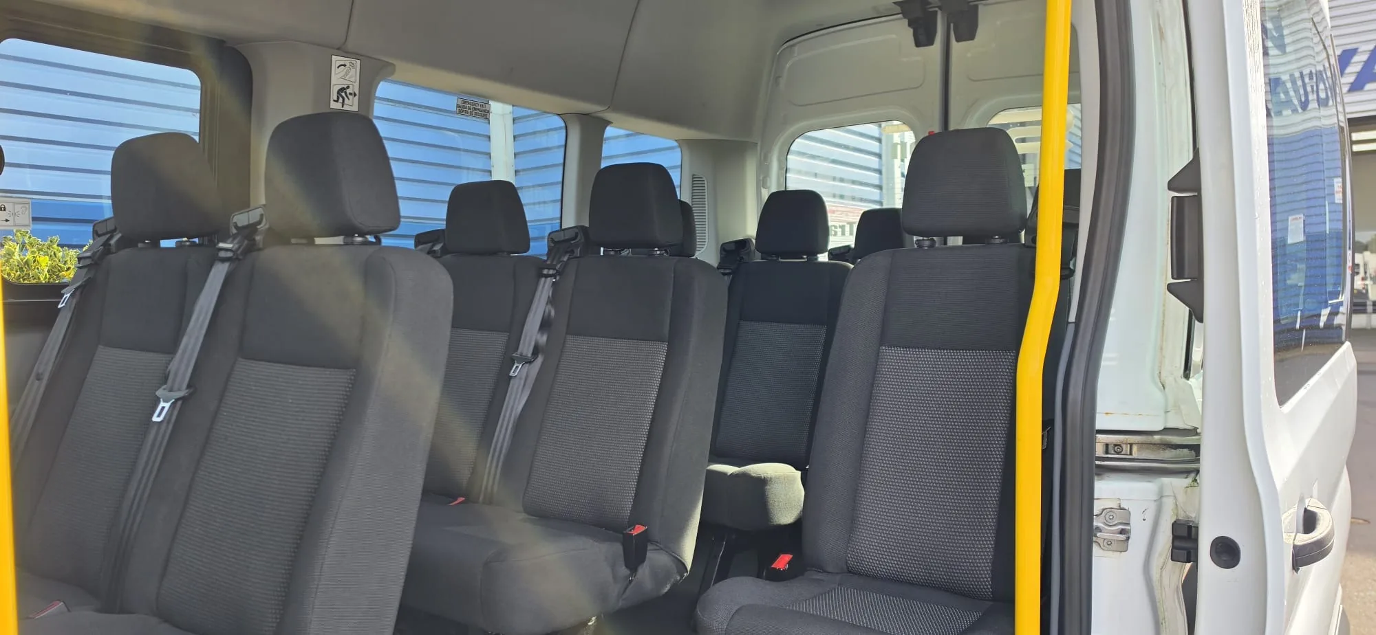 Rows of grey cloth passenger seats with seatbelts inside a 17 seater minibus, seen from the side door