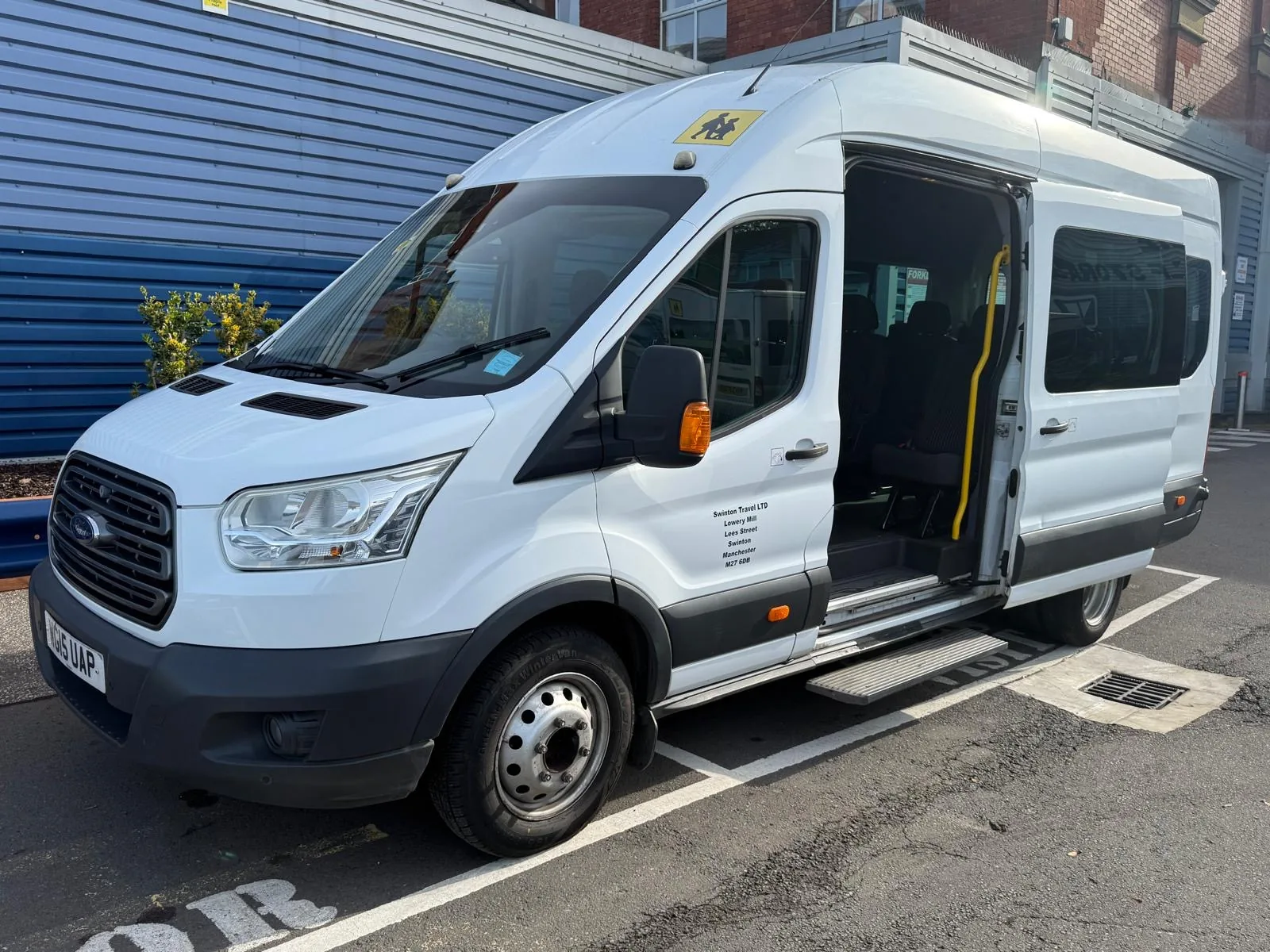White 17 seater Ford Transit minibus with its sliding side door open, showing the step and grab handle