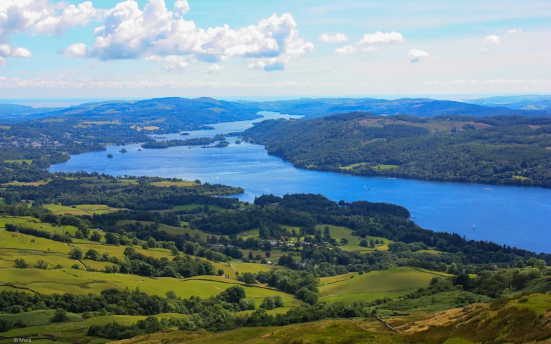 Lake surrounded by rolling green hills under a blue sky in the English countryside