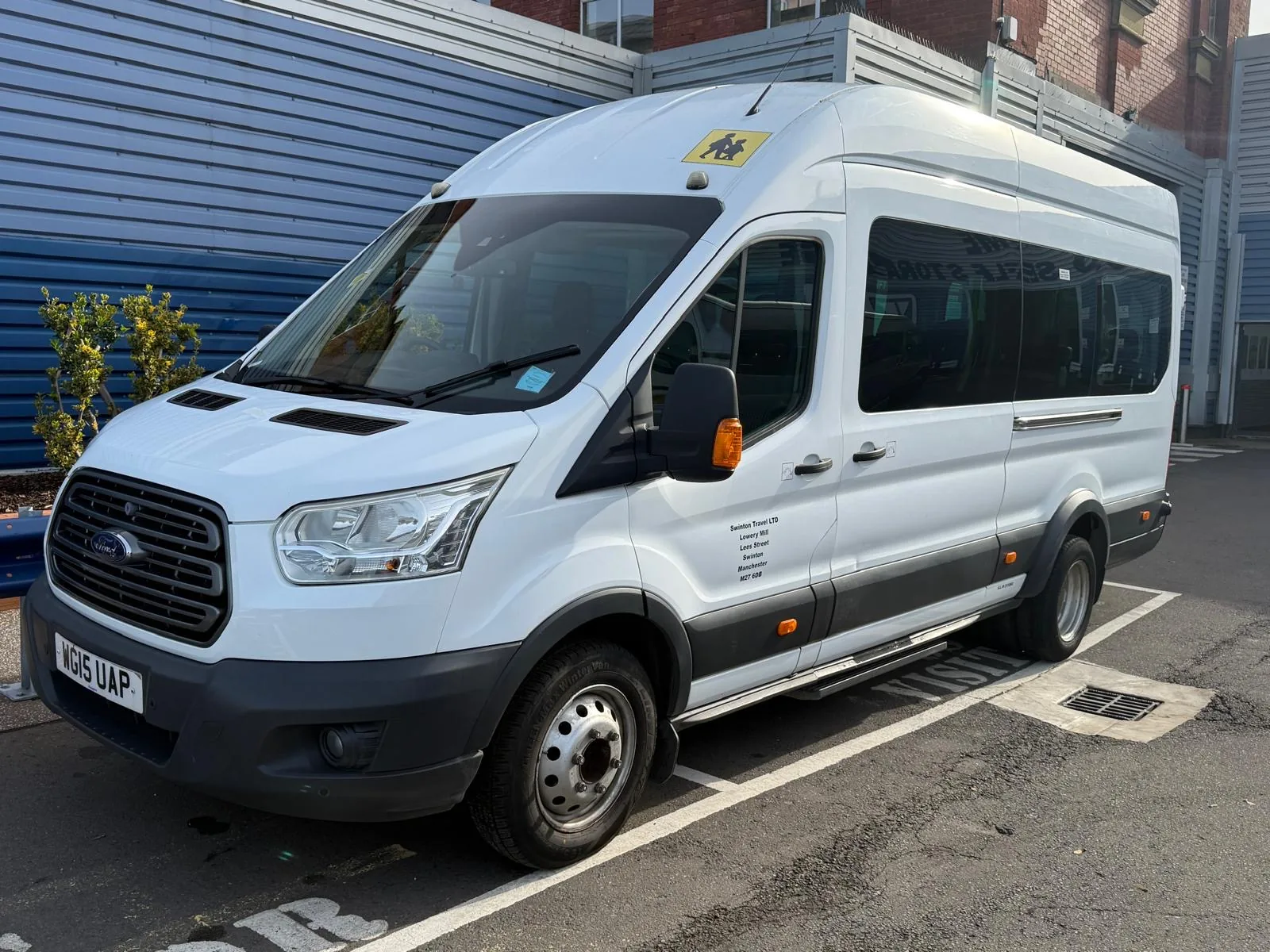 White Ford Transit minibus with a school bus sign and company lettering on the door, front three-quarter view